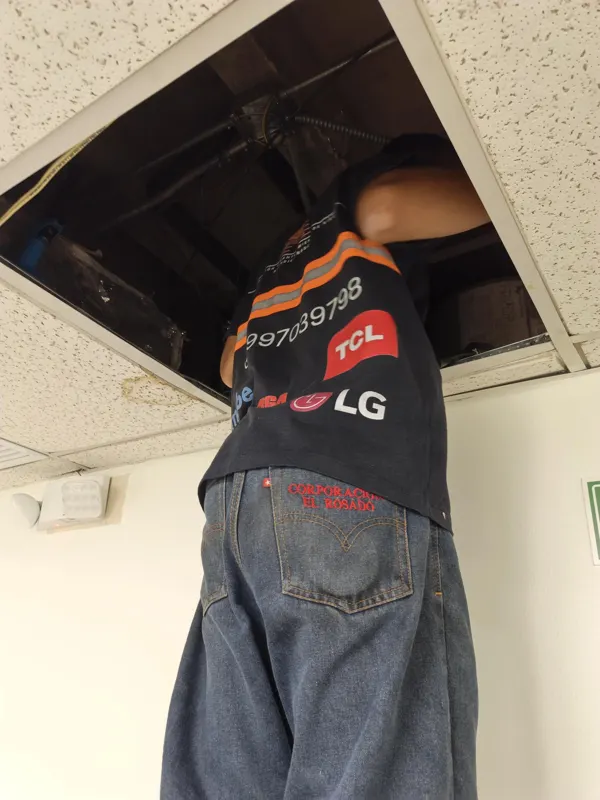Técnico de Alvarado Solutions revisando un equipo de aire acondicionado por ductos sobre el cielo falso de una oficina en Guayaquil